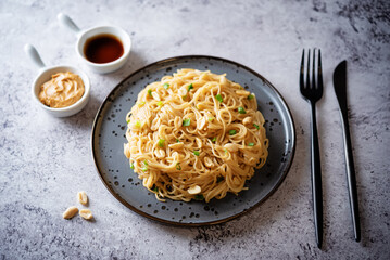 Wheat pasta with peanut butter soy sauce, roasted peanuts and scallion in a plate