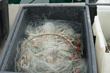 Fishing net with white ropes and red-brown floats stored in black quadrat plastic box ready for...