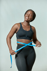 Happy african american young woman measuring waist size with tape measure. Body positive,...