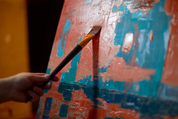 Artist hand holding paintbrush putting brushstrokes on canvas, closeup. Contemporary masterpiece....