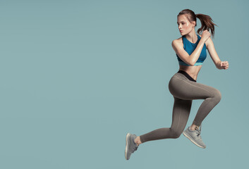 Athletic energetic girl jumping on a blue background.