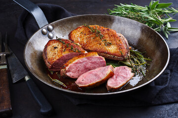 Traditionell gegrilltes Gourmet Entenbrust Filet mit Haut serviert mit Kräutern als close-up in einer rustikalen Bratpfanne