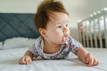 Front view of small healthy caucasian baby three months old boy or girl lying on the bed at home with belly down in bright room with copy space