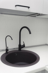 black kitchen sink with white minimalist backsplash, granite countertop, gray cabinets and black...