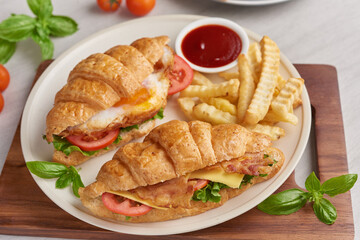 two croissant sandwiches on wooden table, top view, Sandwich with bacon, fried egg. Ham, cheese, bacon, fried egg, tomato, french fries and lettuce served in a plate.