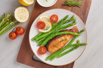 Delicious seasonal green asparagus and sliced smoked salmon on a rustic plate with lemon, salt, pepper, of lemon on a white plate . Baked salmon garnished with asparagus and tomatoes with herbs.