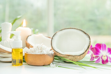 Coconut oil, tropical leaves and fresh coconuts. Spa coconut products on light wooden background. Spa still life of organic cosmetics with coconuts on a light wooden background, body care concept.