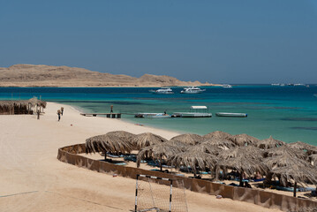 Naklejka premium Holidays in Egypt. Beach with umbrellas made of dry palm leaves, desert and yachts in the blue water of the Red Sea. Vacation and Holidays in Egypt.