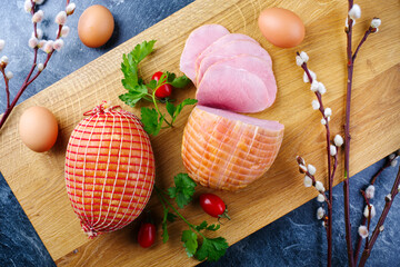 Traditional German boiled Easter ham with tomatoes and eggs offered as top view on modern design wooden board