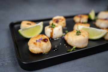 Fried scallops with butter lemon spicy sauce on black plate over old dark stone background.