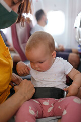 mother with 14 month old baby on plane with seat belt to start trip.
