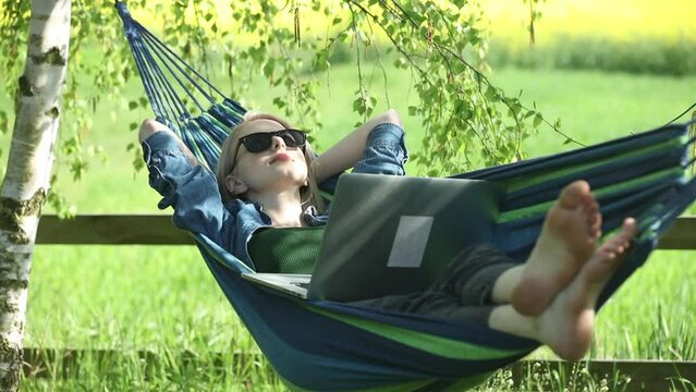Woman in hammock working with laptop computer in hammock in countryside