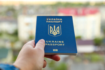 Defocus passport of a citizen of Ukraine in a female hand on a blurred urban background, close-up. Inscription in Ukrainian Ukraine Passport. War. Person. Out of focus