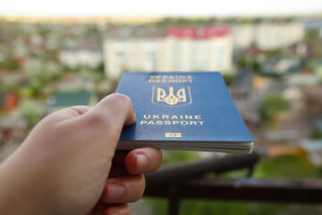 Defocus passport of a citizen of Ukraine in a female hand on a blurred urban background, close-up. Inscription in Ukrainian Ukraine Passport. War. Person, people. Border. Out of focus