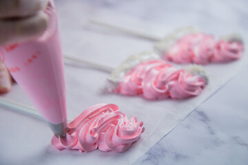 From the pastry bag, the pastry chef squeezes out a zigzag meringue on white parchment and a red...