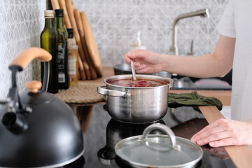 Fototapeta na wymiar Woman in apron cooking delicious borscht soup on the hob