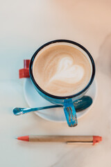 A cup of cappuccino and a pen are on the table in the cafe