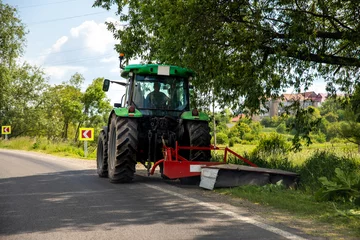 Foto op Plexiglas Big modern industrial tractor machine cutting green grass with mowing equipment along country roadside. Road lawn mower machinery vehicle highway maintenance service outdoors on sunny day © Kirill Gorlov