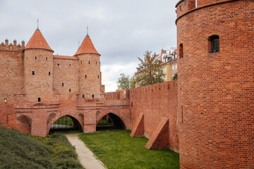Fototapeta na wymiar Warsaw, Poland, 13 October 2021: Barbican complex network of historic fortifications between Old and New Town, red brick fort wall with towers, major tourist attraction at sunny autumn day, city gate