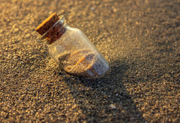 Corked Old Bottle in the sea beach at sunset. Concept of travel background.