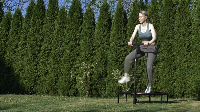 girl does Jumping fitness on trampoline in outdoor on green grass and trees on background