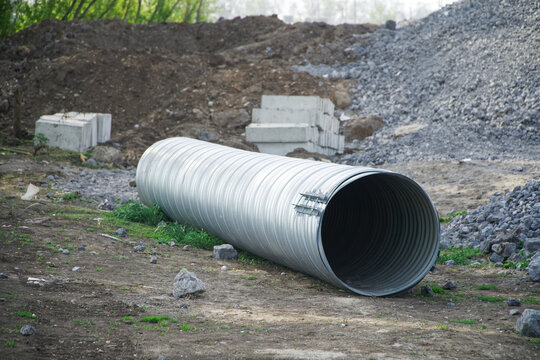 A large corrugated metal pipe with a coupler, prepared for installation, lies on a construction site next to a pile of gravel. Production of storm sewerage