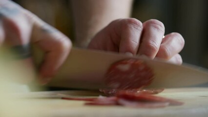 Close up shot of male hands cutting salami into thin slices with knife