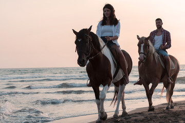 Fototapeta na wymiar a loving couple in summer clothes riding a horse on a sandy beach at sunset. Sea and sunset in the background. Selective focus 