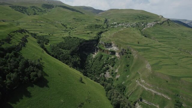 Aerial view of a huge beautiful rock with clouds on the background. Action. Flying above mountains with green slopes.
