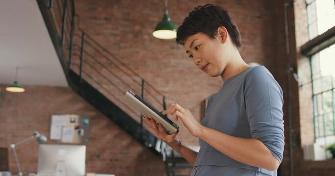 young businesswoman using a digital tablet in a modern office. Focused young asian businesswoman standing in her office using a wireless digital tablet. Young businesswoman using apps on tablet