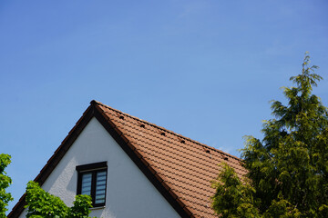 Im Eigenheim wohnen - Im Grünen leben. Dachfirst vmit Fenster on einem Einfamilienhaus umrahmt von hohen Bäumen