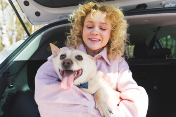 charming blonde European girl hugging her cute dog while sitting in the car trunk medium shot outdoor pets and humans concept. High quality photo