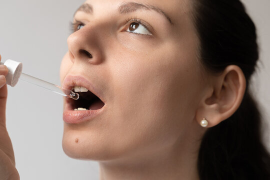 Portrait of dark haired young woman taking oil supplement with glass dropper. CBD hemp medicine oil applying on the tongue 