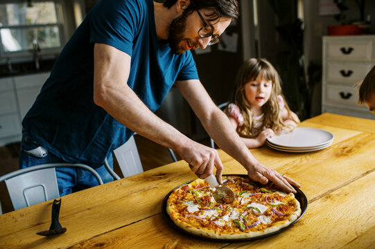 Single dad cutting pizza while his children watch with anticipation