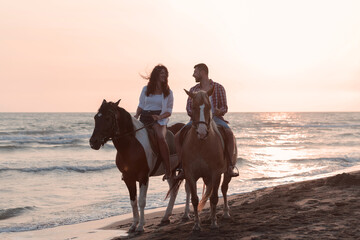 Fototapeta na wymiar a loving couple in summer clothes riding a horse on a sandy beach at sunset. Sea and sunset in the background. Selective focus 