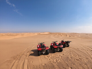 Three quad bikes parked in the middle of the desert near Swakopmund, Namibia, on a big dune with nothing else than a clear blue sky and more dunes in the distance. Vacation, adventure scene.  