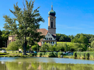Bell tower of the Notre-Dame de Thierenbach basilica church behind a pond and some trees, on a sunny spring day