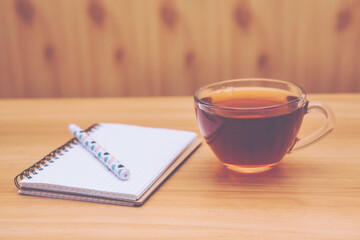 Cup of black tea and notebook with pen on the table, simple still life in vintage style