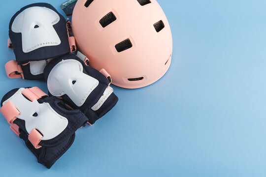 Top View Of Roller Skates Protective Gear Set - Knee, Elbow And Wrist Pads, Helmet In Pink Colors. Blue Background Flat Lay 