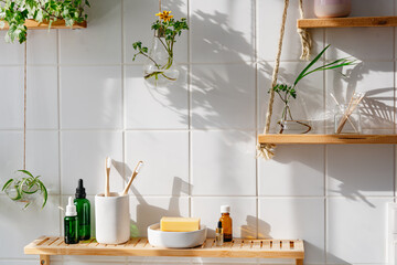 Wooden shelves with cosmetics and toiletries against white tile wall with biophilic design. Hanging glass pots with green plants