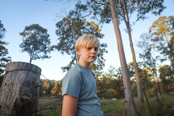 Relaxed boy on farm leaning against fence in golden afternoon light