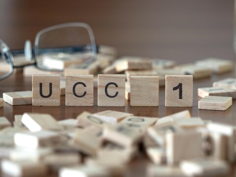 the acronym ucc 1 for uniform commercial code-1 statement word or concept represented by wooden letter tiles on a wooden table with glasses and a book