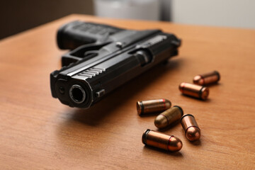 Semi-automatic pistol and bullets on wooden table indoors, closeup