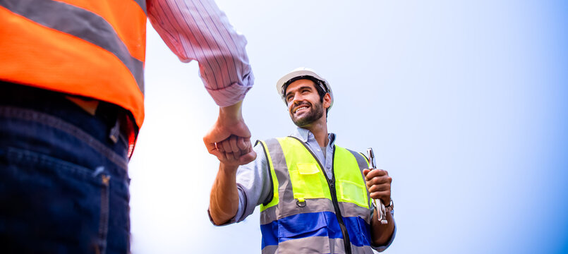 
Handsome European engineers greet each other with fist bumps. Middle Eastern workers smiling with confidence, happy at work, professional, wearing PPE,hard hat,reflective,vest.New normal professional