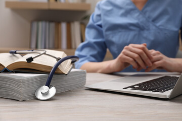 Woman with book, stethoscope and laptop at table indoors, closeup. Medical education