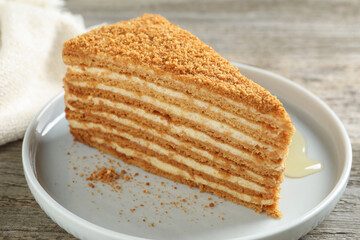 Slice of delicious layered honey cake served on wooden table, closeup