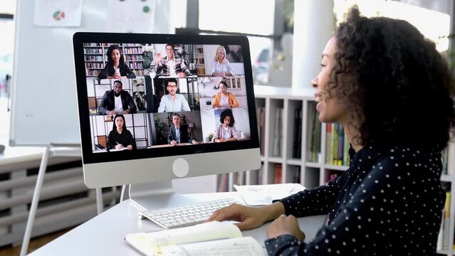 Video conference. Successful African American woman, company worker, sits at a work desk in front of a computer, takes an online brainstorm, business conversation with multiracial group of people