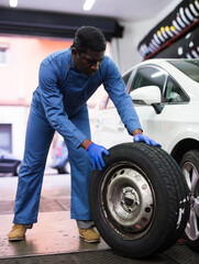 Mechanic engaged in replacement of tyre on car wheel in auto workshop