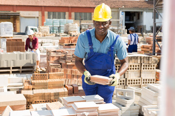 Focused african american man working in a building materials store lays tiles in an open air...