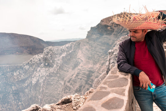 Mestizo latin man taking a selfie with his smartphone wearing a colorful hat looking towards the crater of the Masaya volcano in Nicaragua. Adventure and travel photo